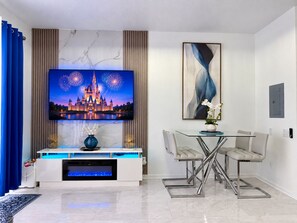 A modern living room with a flat-screen TV, a dining area with a glass table, and a fireplace. - Luxury Remodel Townhome 3 bedroom 3 bathroom,Near Disney with Private Pool (Kissimmee)