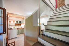 A modern kitchen with green cabinets, a central island, and a staircase with glass railings. - Casa Greta - Flo Apartments (Montespertoli)