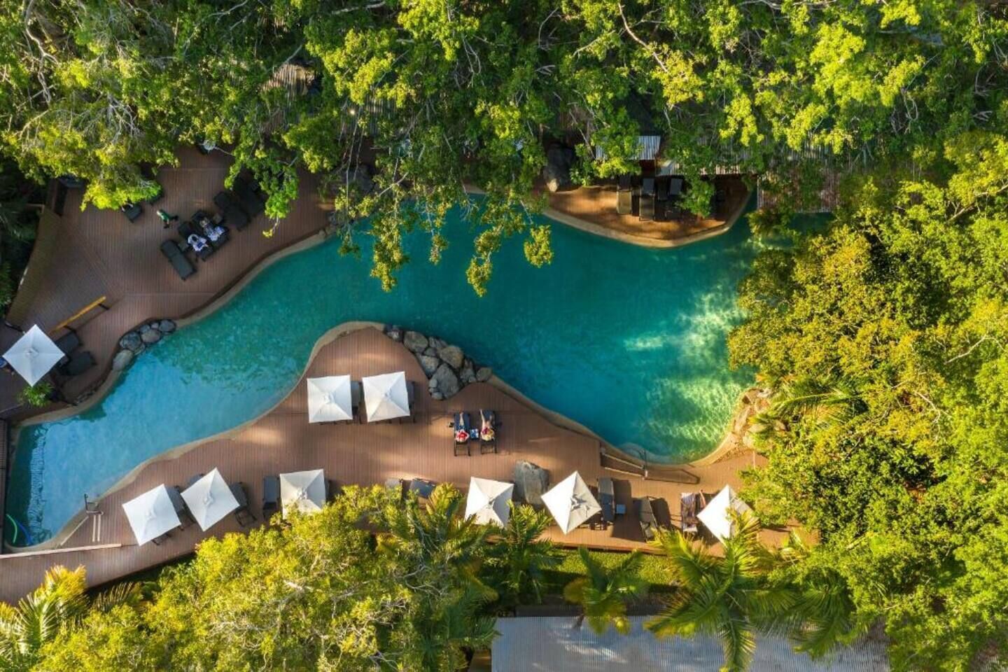 An aerial view of a resort with a swimming pool, lounge chairs, and umbrellas.