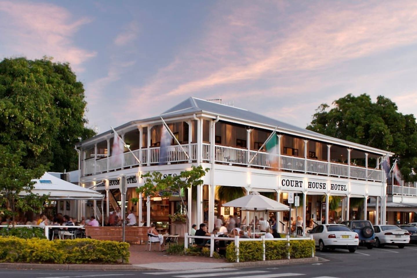 A two-story building with a balcony, labeled 'COURT HOUSE HOTEL,' featuring outdoor seating and a parking area.