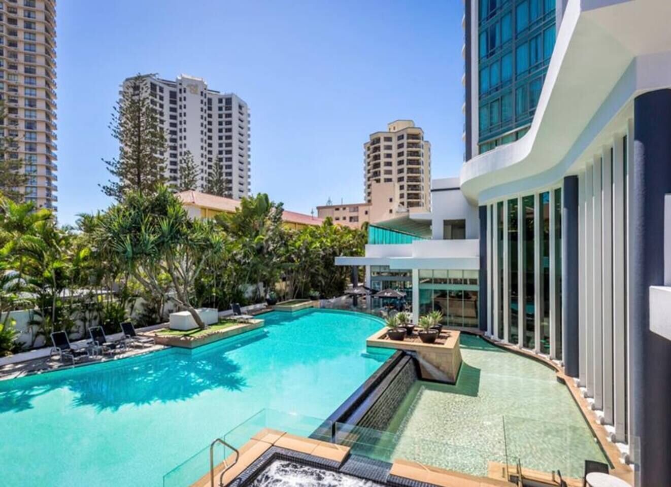 A swimming pool with lounge chairs, surrounded by tall buildings and greenery.