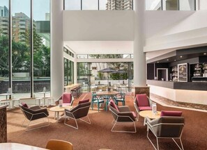 Eine moderne Hotelhalle mit hoher Decke, großen Fenstern, einer Bar und Sitzgelegenheiten.