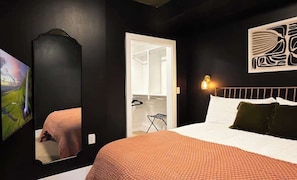 Ein Schlafzimmer mit Bett, Kleiderschrank, Spiegel und einem Wandbild.
