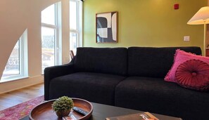 Ein modernes Wohnzimmer mit einem dunkelgrauen Sofa, einem rosafarbenen Kissen und einem Couchtisch mit Pflanze und Fernbedienungen.