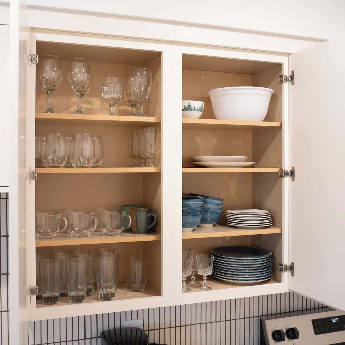 Un armario de cocina con estantes que contienen diferentes vasos y vajilla.