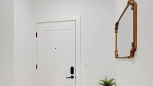 Eine weiße Tür mit schwarzem Griff, ein kleiner Holztisch mit Pflanze und ein Spiegel an der Wand.