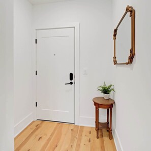 A white door with a black handle, a small wooden table with a plant, and a mirror on the wall. - Fifa Stay 5 Min Walk Met Sleeps 5 3 Beds Gym (Philadelphia)