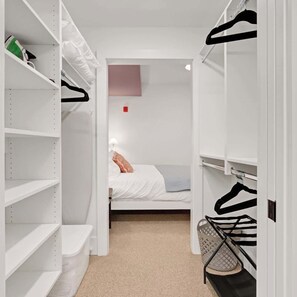 A walk-in closet with open shelves, a bed with a white comforter, and a hanging rack with clothes. - Fifa Stay 5 Min Walk Met Sleeps 5 3 Beds Gym (Philadelphia)