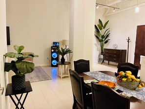 A dining area with a table set for two, a speaker with illuminated lights, and a potted plant.