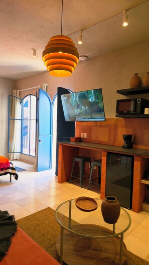 Ein modernes Wohnzimmer mit Flachbildfernseher, Glastisch und Küchenzeile inklusive Mikrowelle.