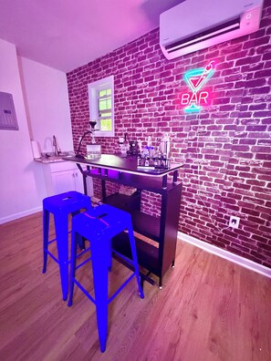Eine Küche mit Ziegelwand, einer Neon-Bar-Beschilderung und zwei blauen Barhocker.