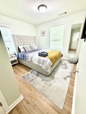 Ein Schlafzimmer mit einem Bett, einem Nachttisch, einem Spiegel und einem Fenster.