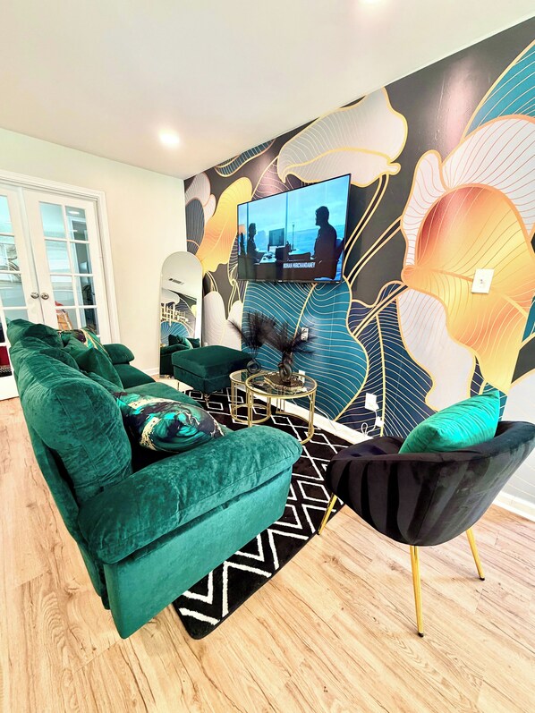 Ein modernes Wohnzimmer mit einem grünen Sofa, einem schwarzen Sessel, einem Glastisch und einem an der Wand befestigten Fernseher.