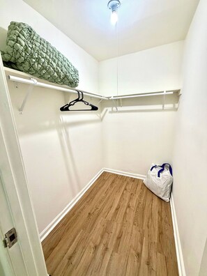 Ein kleiner, gut beleuchteter Kleiderschrank mit Holzboden, einer Kleiderstange und einer Tasche auf dem Boden.