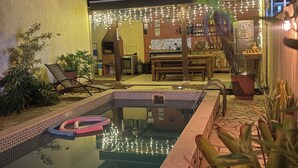 A swimming pool with a stone border, surrounded by potted plants and outdoor furniture. - Flats Brisapart (Ubatuba)