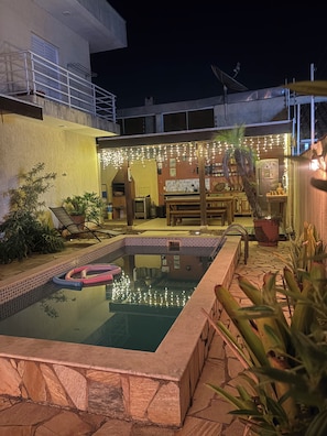 A swimming pool with a stone border, surrounded by potted plants and outdoor furniture.
