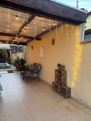 Une terrasse extĂ©rieure agrĂ©mentĂ©e de guirlandes lumineuses, dâune piscine et de plantes en pot.