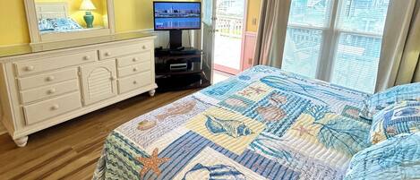 A bedroom with a bed, dresser, television, and a view of the outside.