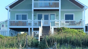 Une maison de plage à deux étages, dotée d’un balcon, d’une porte d’entrée et d’un numéro, le « 199 », bien visible sur le côté.