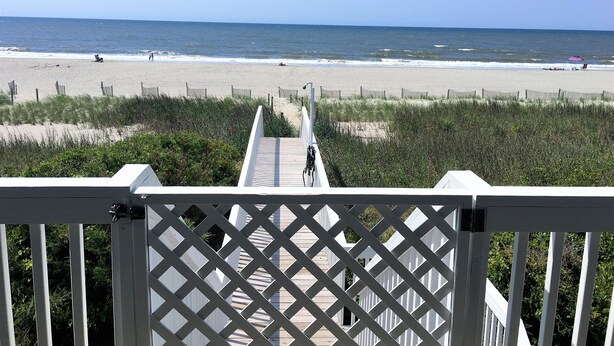 Une terrasse en bois qui mène à une plage et offre une vue dégagée sur l’océan.