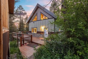 A modern cabin with a deck, surrounded by dense forest. - Two Top Stop | 15min to Yellowstone, Hot Tub, Arcades, BBQ! (Island Park)