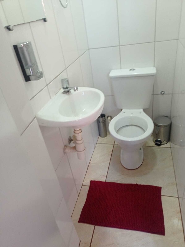 A bathroom with a white sink, toilet, and a red rug on the floor.
