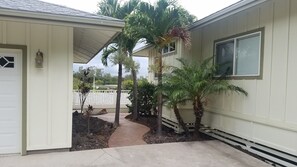 Ein Haus mit überdachter Veranda, Garage und einem kleinen Garten mit Palmen.