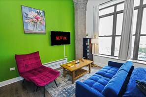 A modern living room with a green wall, a red chair, a blue sofa, and a television displaying the Netflix logo. - McCormick Place Modern Suite for 4, with Optional Parking (Chicago)