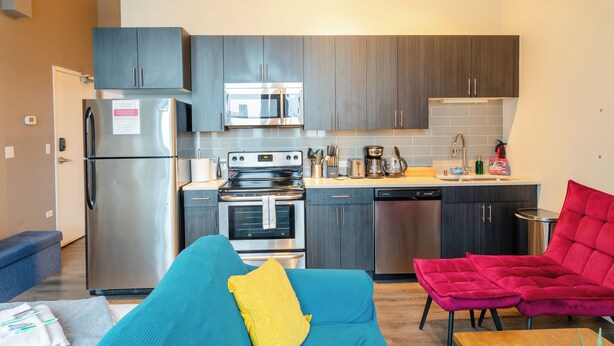 A compact kitchen with modern appliances, a dining area with a blue sofa and a red chair, and a small dining table. - McCormick Place Modern Suite for 4, with Optional Parking (Chicago)