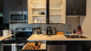 A modern kitchen with dark cabinetry, a stainless steel stove, a microwave, and a dishwasher. - McCormick Place Modern Suite for 4, with Optional Parking (Chicago)
