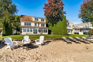 En ejendom ved stranden med et stort hus, udendørs siddepladser og en bålplads.