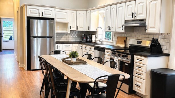 Una cocina moderna con armarios blancos, electrodomésticos de acero inoxidable, una mesa de comedor de madera y sillas negras.