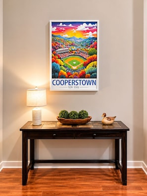 Ein gerahmtes Poster von Cooperstown, New York, auf einem dunklen Holzkonsole mit einer Lampe und Dekorationsgegenständen.