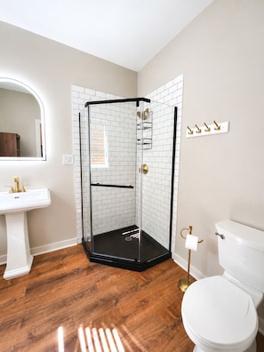 A bathroom with a glass shower enclosure, white tiles, a white sink, a toilet, and a mirror.