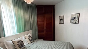 Ein Schlafzimmer mit Bett, Nachttisch, Vorhängen, einem Holzschrank und zwei Wandbildern.