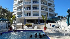 Ein mehrstöckiges Hotel mit Schwimmbad, Sitzgelegenheiten im Freien und blauem Himmel.