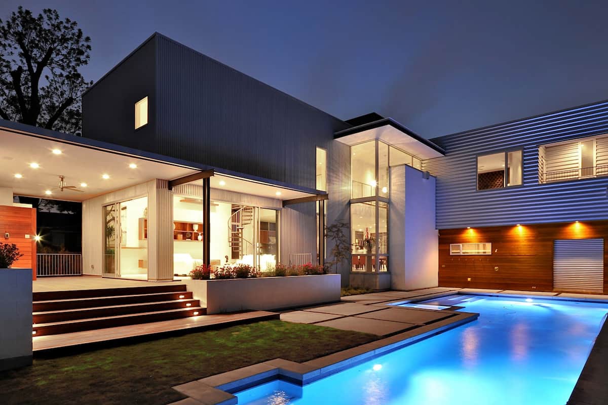 A modern house with a swimming pool, large windows, and a well-lit interior.
