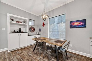 A dining area with a wooden table, metal chairs, a chandelier, a window with a view, and a wall with a space-themed painting.
