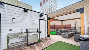 An outdoor patio with a grill, seating area, and a brick wall. - Space City Retreat  Rooftop Views Fire Pit Putting Green Sleeps 8 (Houston)