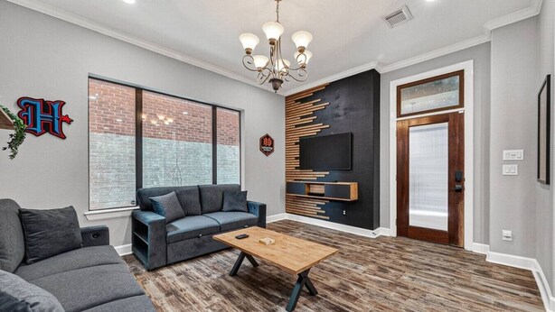 A modern living room with a sofa, coffee table, TV, and a brick wall. - Space City Retreat  Rooftop Views Fire Pit Putting Green Sleeps 8 (Houston)