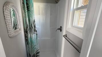 Un petit espace douche fermé, doté d’une porte en verre, d’une fenêtre sur le côté droit et d’un rideau de douche à motifs.