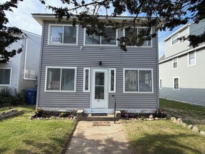 A two-story residential building with a front entrance, a small front yard with a pathway, and a mailbox. - 3-bedroom 1st Floor cottage unit 100 yards from beach (Old Lyme)