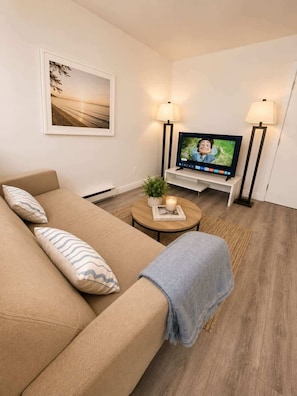 Uma sala de estar com sofá, mesa de centro, televisão e duas luminárias de chão.