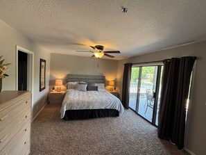 A bedroom with a bed, two bedside tables, a ceiling fan, a large window with curtains, and a view of a body of water. - Waterfront Lake Escape - Pool, Dock, Sunset Views (Osage Beach)