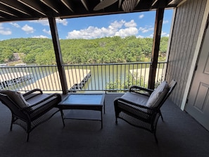 A balcony with wicker furniture, a view of a river, and a forested hill.
