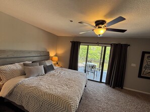 Une chambre avec un grand lit, un ventilateur de plafond et une vue sur un espace extérieur aménagé avec une table et des chaises.