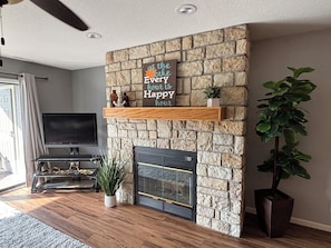 A living room with a stone fireplace, a flat-screen TV, a wooden entertainment unit, and a large potted plant.
