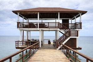 A multi-level wooden pier with railings, a covered upper deck, and a view of the sea. - Xanadu Resort Roatan (Sandy Bay)