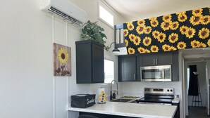 Cocina moderna con armarios oscuros, un microondas, un horno y un lavaplatos. Hay una pequeña isla con una bolsa etiquetada 'Snacks' y una planta encima.