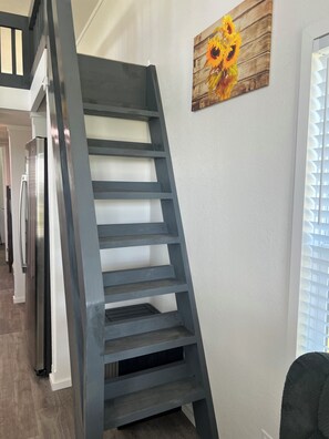 A modern interior with a grey metal staircase, a wooden wall art piece, and a kitchen area. - The Sunflower Villa - 15 Miles from the Beach! (Foley)